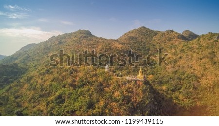 Aerial view above golden Pagoda on the hill around with green forest and blue sky background, Wat Ban Tham, Tha Muang District, Kanjanaburi, west Thailand.