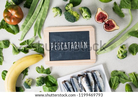 a signboard with the text pescatarian, for vegetarian people who eat fish, and a pile of some different fruits and raw vegetables, and a pile of sardines in a plate, on a white stone countertop Royalty-Free Stock Photo #1199469793