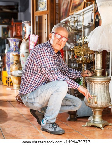 Interested mature male collector of rare goods choosing ancient things in antique shop
