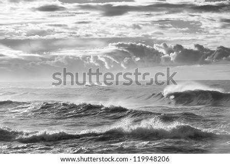 Black and white photograph of a wave breaking beneath a storm sky