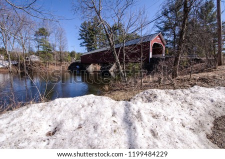 The Carlton Covered Bridge in Swanzey New Hampshire crosses the Ashuelot River. Photo taken in spring with a snowbank in foreground