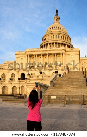 A tourist taking picture of Capitol Building at sunset with mobile phone