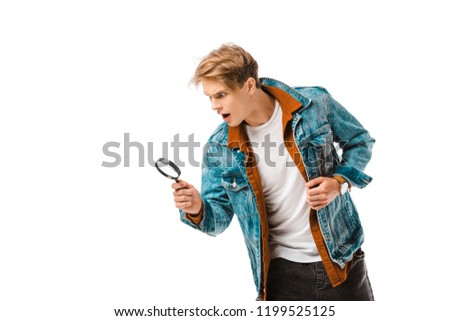 shocked young hipster man looking at magnifying glass isolated on white