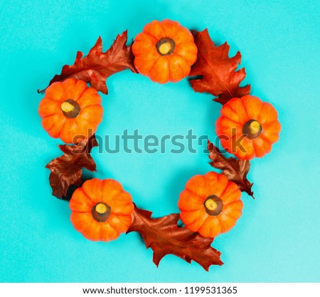 Halloween holiday or autumn background. Five orange pumpkins in a shape of the ring with red dried oak leaves on blue background. View from above. Copy space for text.