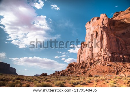 Closeup of Elephant Rock taken from Monument Valley floor. Desert landscape of large sandstone butte, red sand, dry  grass, blue sky and white clouds background. Utah-Arizona border, U.S. of America Royalty-Free Stock Photo #1199548435