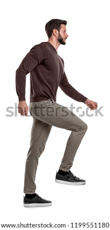 An isolated bearded man in casual wear steps up with one leg in a side view on a white background. Invisible stairs. Moving up in life. Walk to new opportunities. Royalty-Free Stock Photo #1199551180