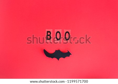 Boo written in black letters next to the bat on a red background. Halloween decoration concept. Top view, flat lay, copy space