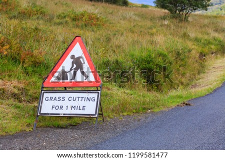 UK Triangle road sign warning of grass cutting for one mile