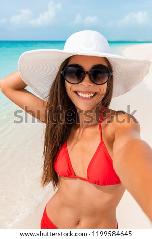 Happy girl taking selfie in summer beach vacation smiling of fun on tropical Caribbean holidays. Asian woman holding camera phone taking picture outside.