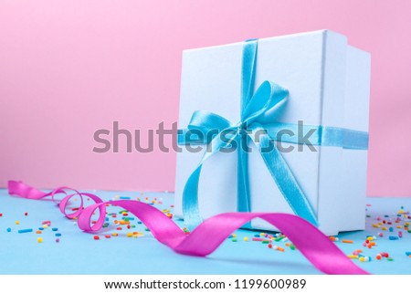 Gift, small box tied with a satin blue ribbon on a pink background. Gift concept. Surprises and gifts for loved ones, congratulations on holidays, give gifts. Copy space 