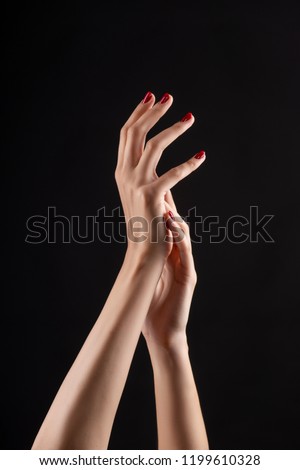 Closeup of beautiful woman hands with red manicure on the nails. Cream for palms, manicure and beauty treatment. Elegant and graceful arms with slender graceful fingers. Copy space. Isolated on black.
