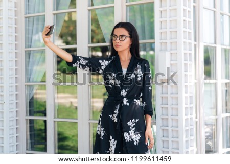 Close-up of a beautiful young girl in a stylish suit standing outside, making selfie on her smartphone. Concept of gadgets, people of technology.