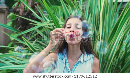 girl teen brunette blowing soap bubbles against a tropical park background.