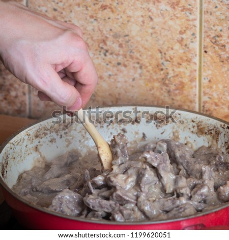 Frying pan on stove with slices of beef meat, oil, sour cream and pepper. Preparation of beef stroganoff. Closeup