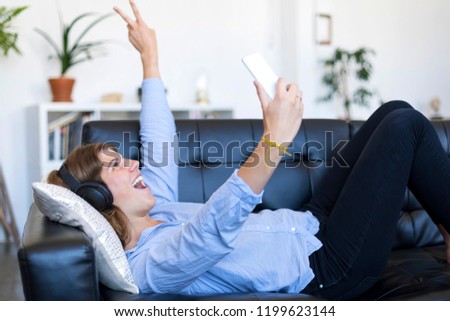 Young pretty long hair woman lying on her back on sofa making selfie on her phone