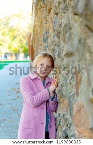 A young girl in a pink coat is leaning against a wall, rubbing in close up