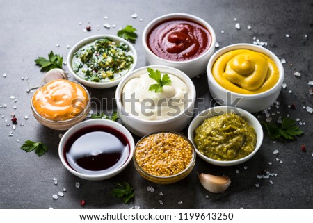 Set of sauces - ketchup, mayonnaise, mustard soy sauce, bbq sauce, pesto, chimichurri, mustard grains and pomegranate sauce on dark stone background. Royalty-Free Stock Photo #1199643250
