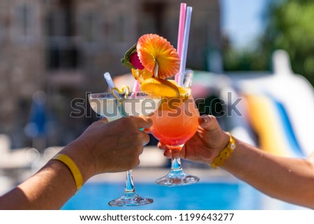 Two beautiful women in red and black bikinis drink colorful cocktails by the pool