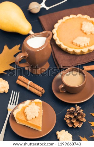 Piece of pumpkin pie with cinnamon and coffee with milk in brown dishes on black background with autumn yellow leaves - top view close up photography of seasonal american traditional sweet baked food.