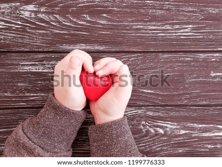 baby hands hold red heart on wooden background