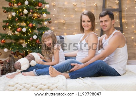 Beautiful dad, pregnant mom, daughter, has happy fun smiling face, blonde hair, dressed in white t-shirt. Portrait home in Christmas. Family kids style. Fashion holiday. 