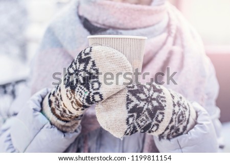 Hot drink in woman's hands wearing warm knitted gloves on cold winter snowy day.