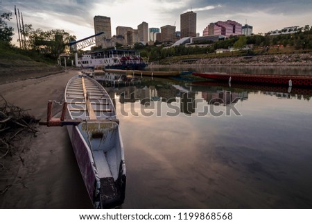 A wide angle view of a dragon boat docked on the river. The skyline is in the background.