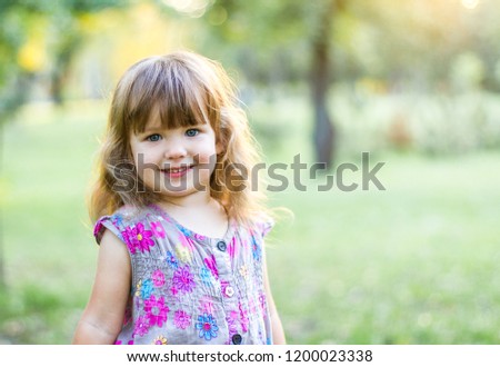 A beautiful little girl is standing in the sun in the park.