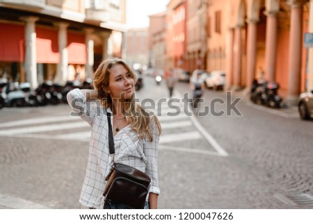 Blonde fashion model wearing jeans and white shirt posing in the street. Italy Bologna, September