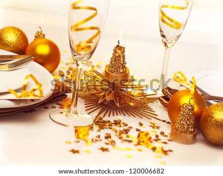 Picture of Christmas romantic table setting, two glasses for champagne adorned with golden ribbon, beautiful little candle, gold shiny bauble, holiday dinner in restaurant, New Year party