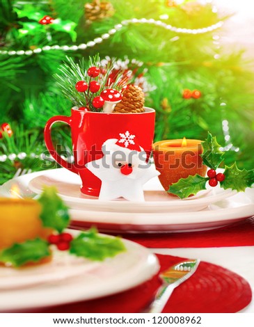 Picture of Christmas eve table setting with beautiful holiday decorations, white and red festive utensil, warm yellow candle light, Santa Claus star toy, little berry branch, New Year party