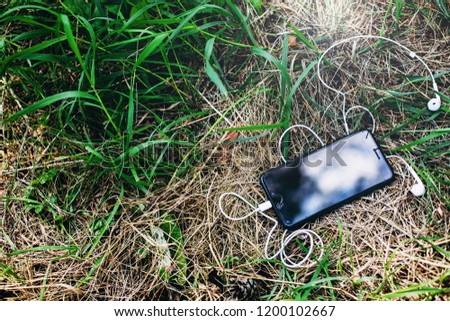 A broken / lost phone with headphones lies in the grass.