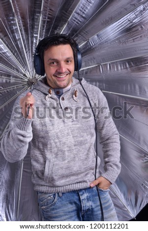 Young man holding a silver umbrella in the studio, smiling, being enthusiastic.