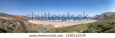 Panorama image of a beach or bay on the atlantic ocean with sand, grass, waves, high rocks and a blue sky with clouds on a sunny day in summer