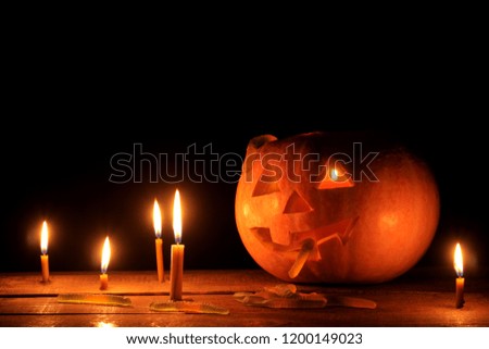 The concept of the holiday of Halloween. Halloween pumpkin head with candles inside and around on a wooden table on a black background