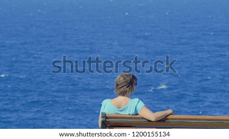 Young Woman Sitting On A Bench Looking At The Blue Mediterranean Sea, Enjoying The Sun And The Tranquility.
