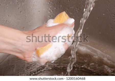 Sponge for washing utensils in the hands of a kitchen sink faucet water