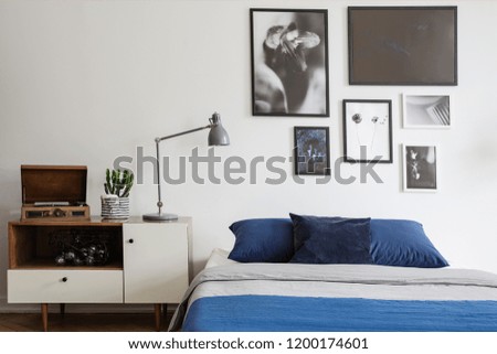 Scandinavian style, wooden dresser by a navy blue bed and framed art gallery on a white wall of a creative bedroom interior