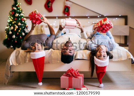 Group of mix raced friends celebrating christmas together. Lying on bed with christmas hats on their heads and looking at camera.