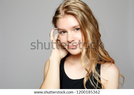 Attractive young girl touching her face. Photo of blonde girl with perfect skin on grey background. Beauty and Skin care concept. Beautiful young woman with natural makeup and clean skin