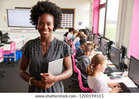 Portrait Of Female Teacher Holding Digital Tablet Teaching Line Of High School Students Sitting By Screens In Computer Class Royalty-Free Stock Photo #1200194515