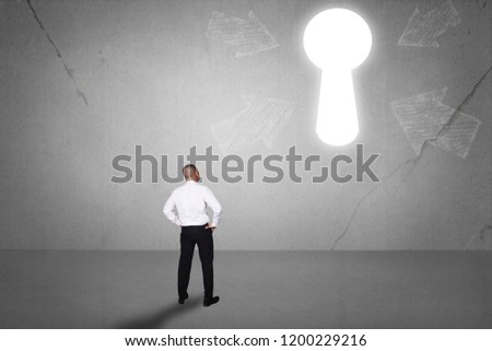 Rear view of businessman facing light keyhole on the wall. Concept of business challenge. Success future hope conquering adversity
