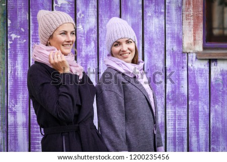 Two cheerful girlfriends are smiling and posing against the bright blue wall. The concept of female friendship. Girls in the same clothes on a warm autumn day
