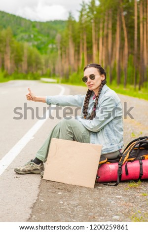 girl travels hitchhiking with a cardboard sign in her hands. Space for text