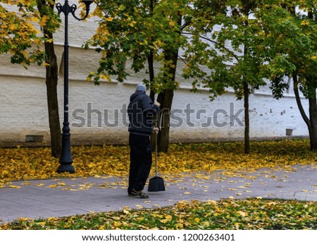 Janitor. A man with a broom removes autumn foliage from the streets. Royalty-Free Stock Photo #1200263401