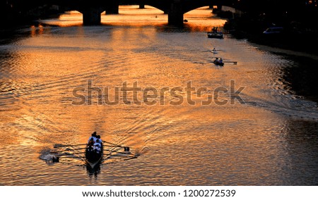 bridge Ponte Vecchio in background and men paddling on a small boat with water reflections in warm sunset on river Arno in florence, italy