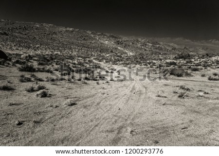 Desert dirt road leading towards hills under black sky. Black and white infrared image.