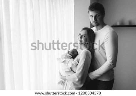 black and white picture of family carrying little baby boy in front of curtains at home