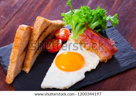 Image of a plate with fried eggs with  bacon, toasted bread and  tomatoes at plate, american breakfast