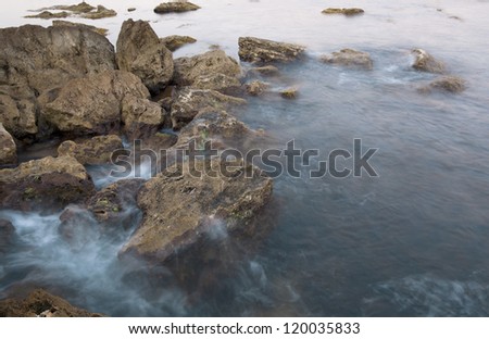 The sea coast with stones, blue water and a surf